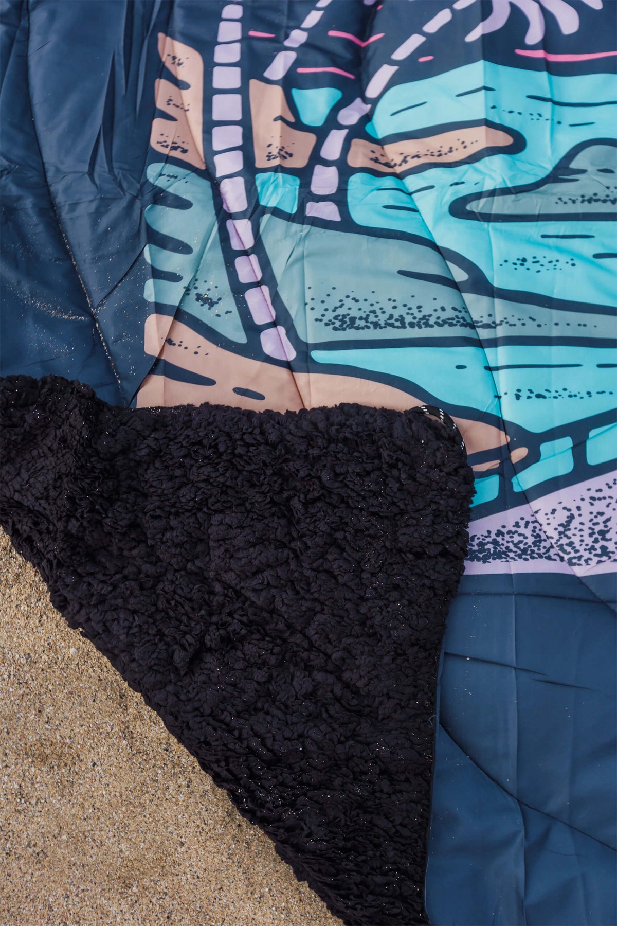 Close-up of a camping blanket with black fleece and colourful patterned design.