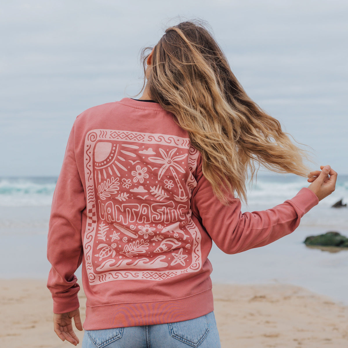 Person wearing a rose sweatshirt with a design on the beach