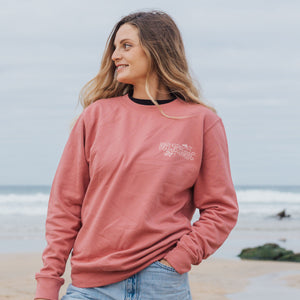 Woman wearing a rose sweatshirt with a logo on a beach